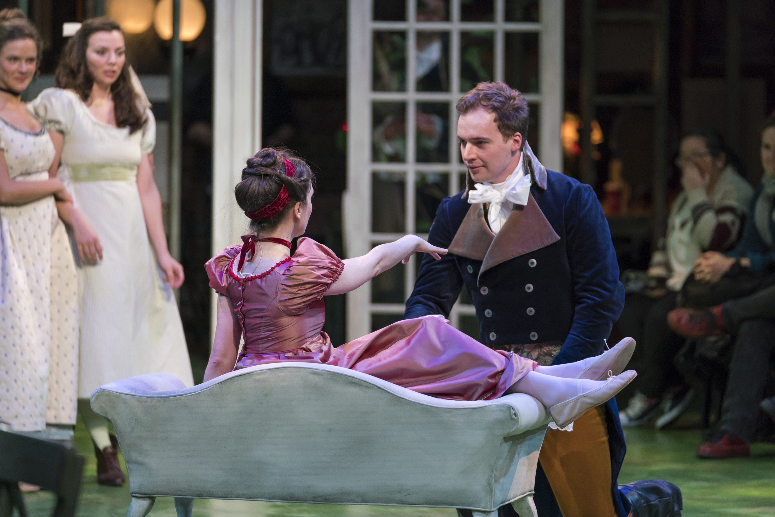 Actor kneels before actress with arm extended on love seat.