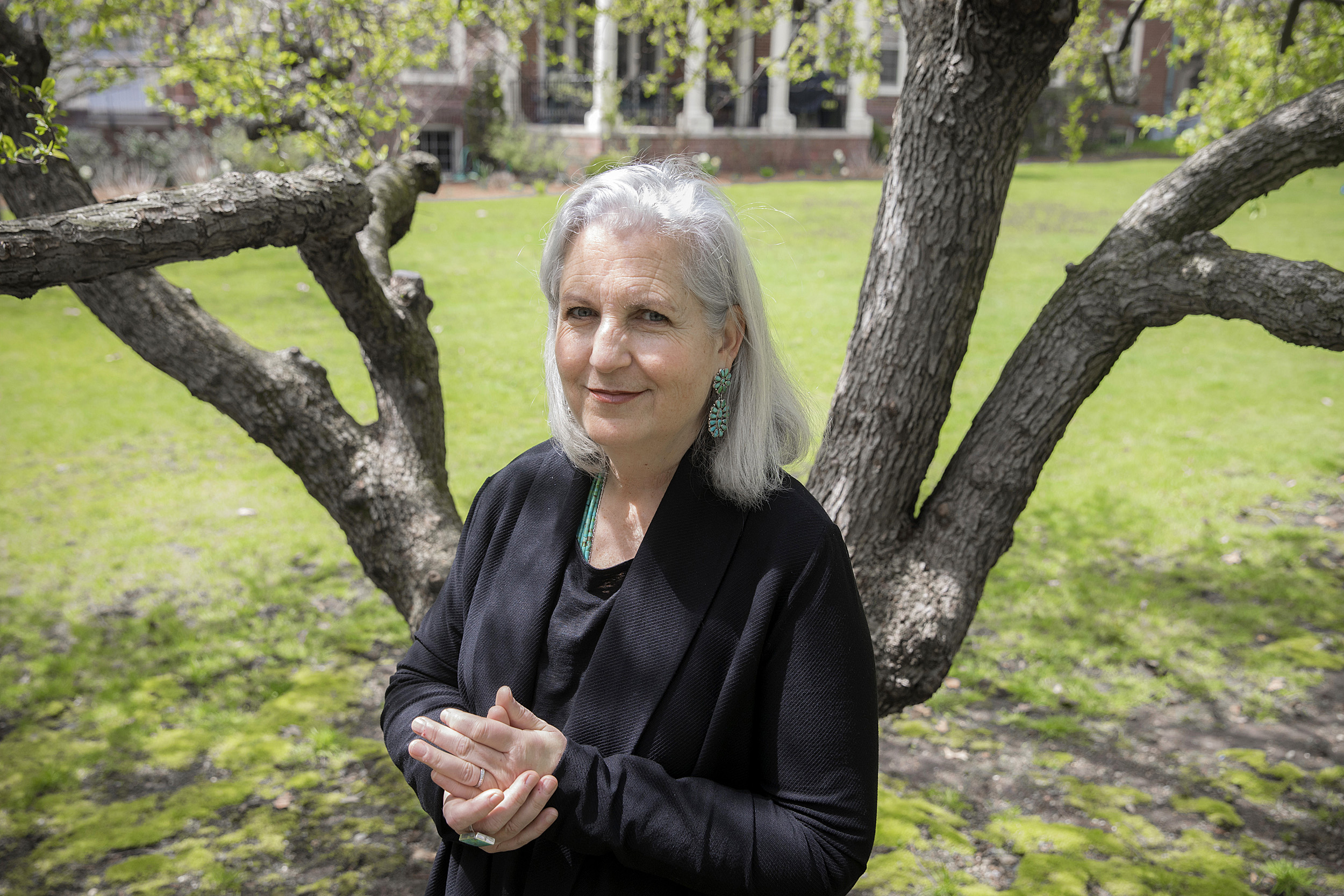 Terry Tempest Williams stands with hands clasped in front of a tree.