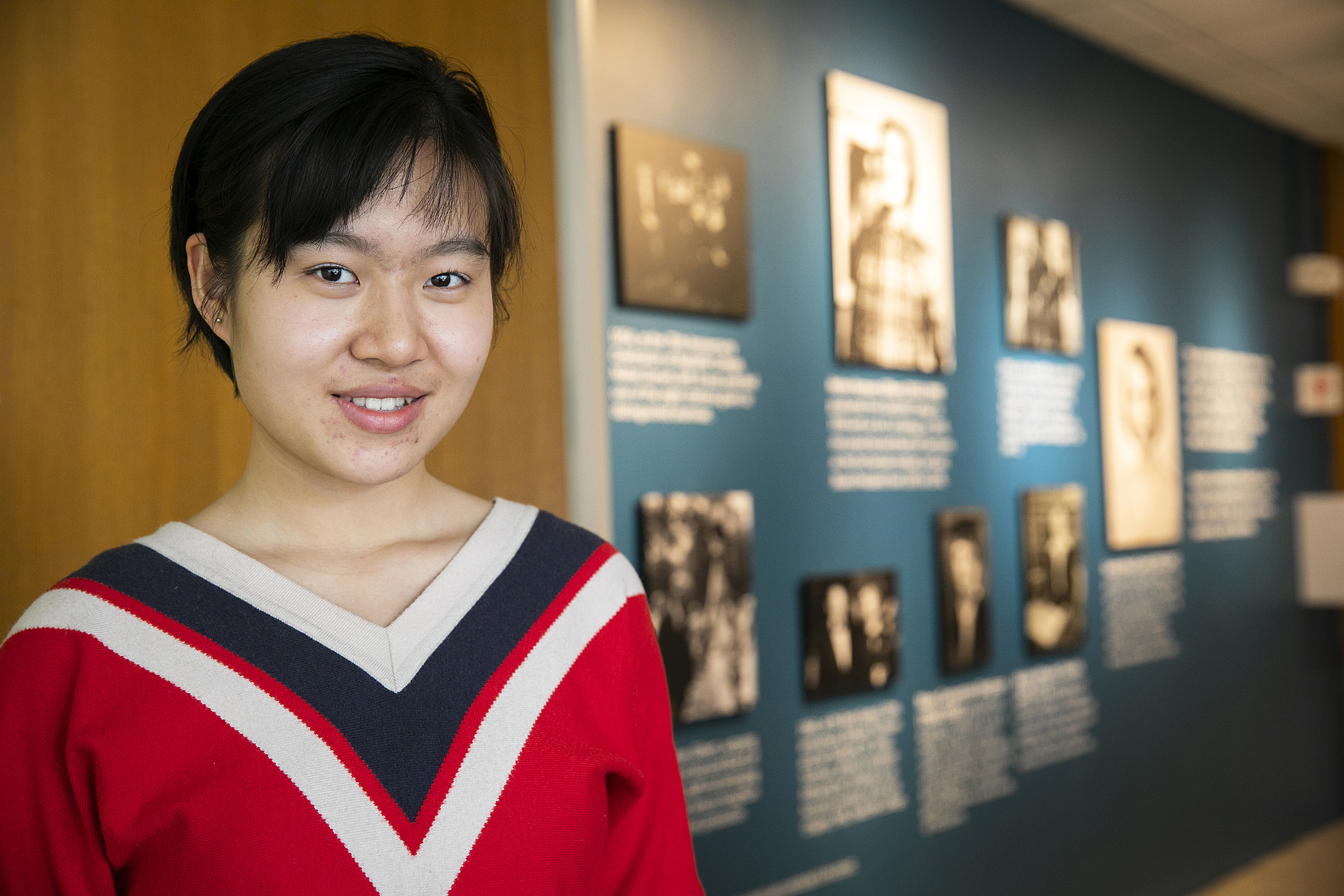 Xue (Snow) Dong in front of the photo wall in Currier House