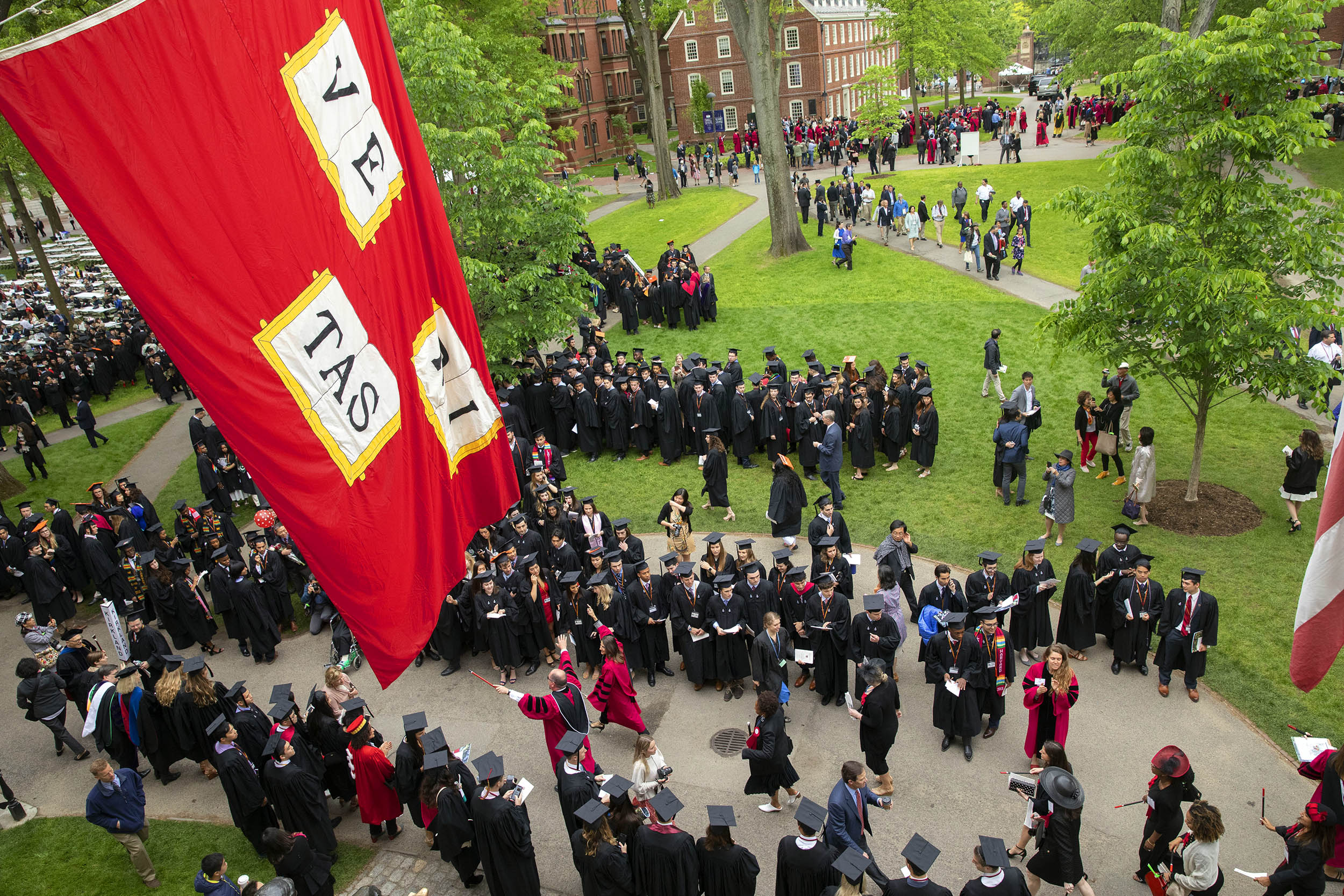 Seniors process past the John Harvard Statue and under the Veritas flag.