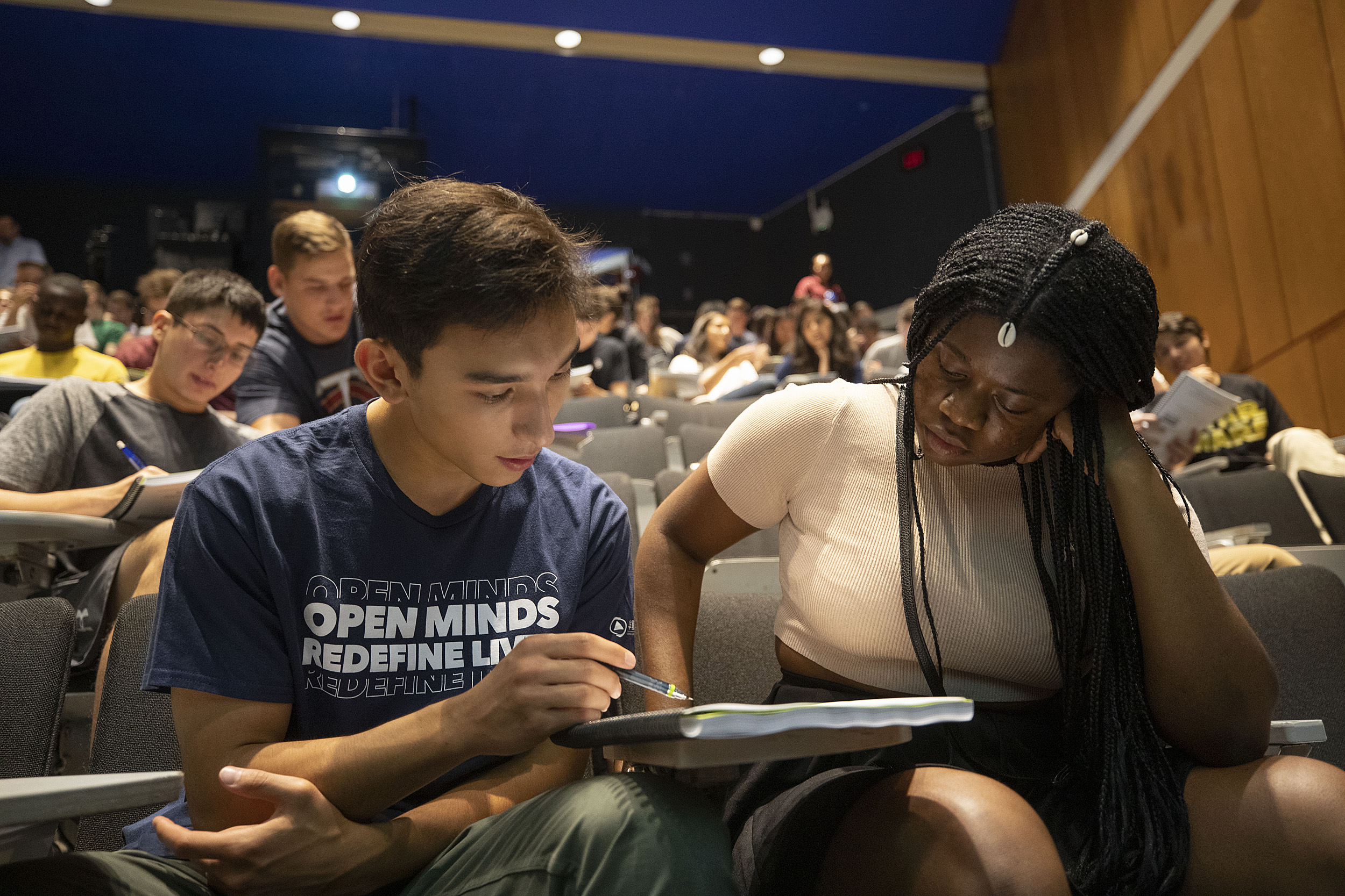 Two students in lecture hall sharing notes.