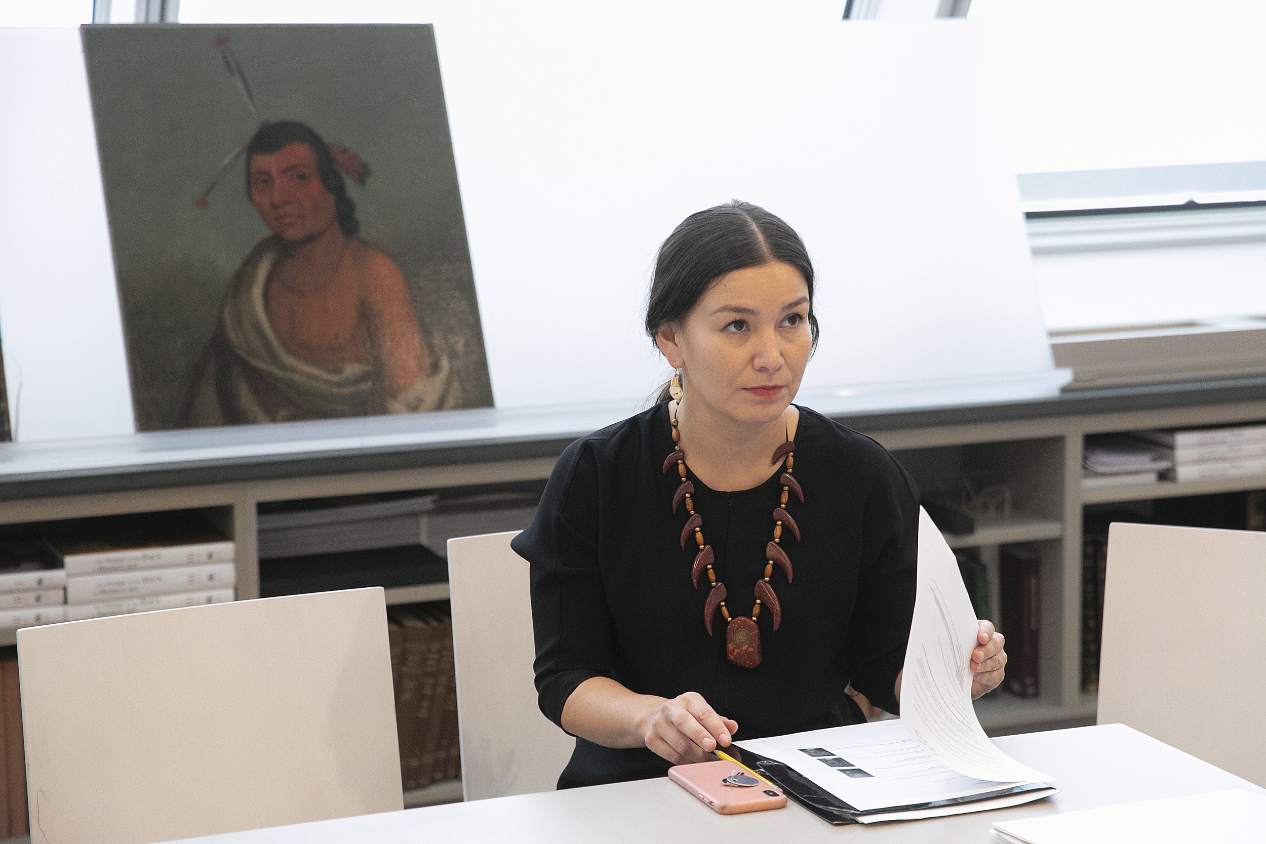 Professor looks up from papers on her desk; a portrait is behind her