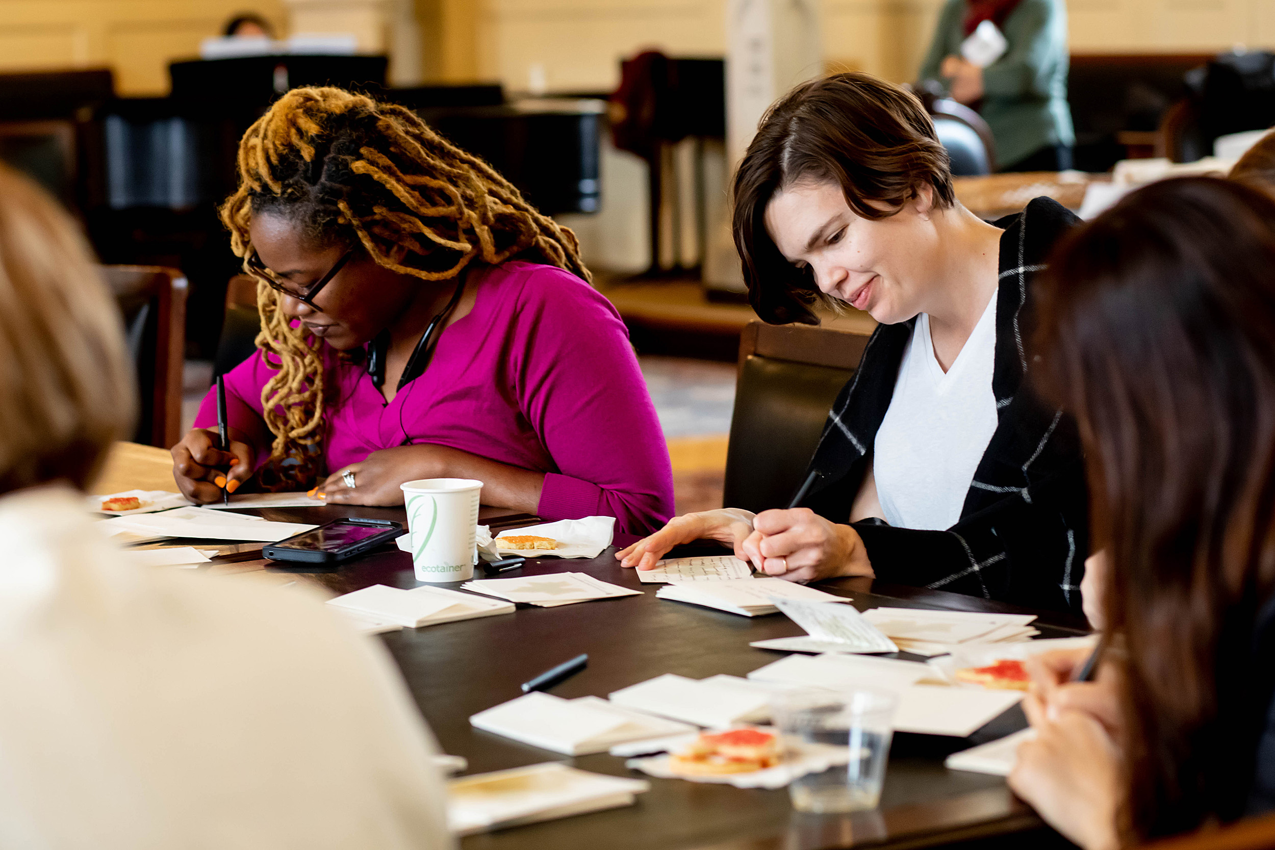 women writing thank-you notes at table.