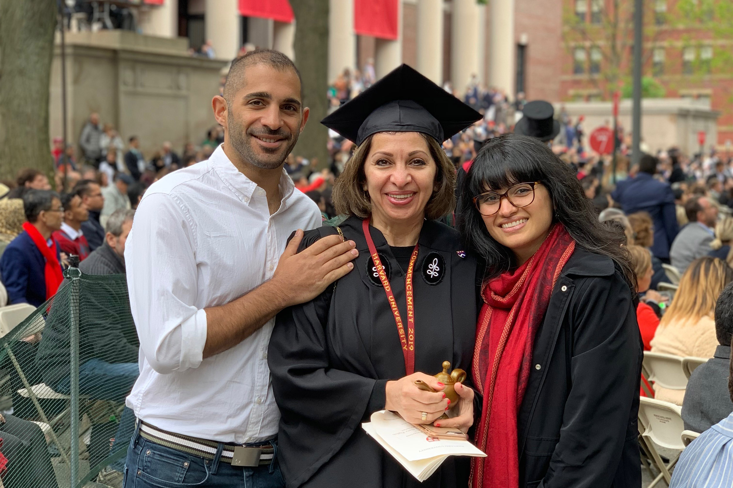 Woman in cap and gown at graduation, flanked by two people.