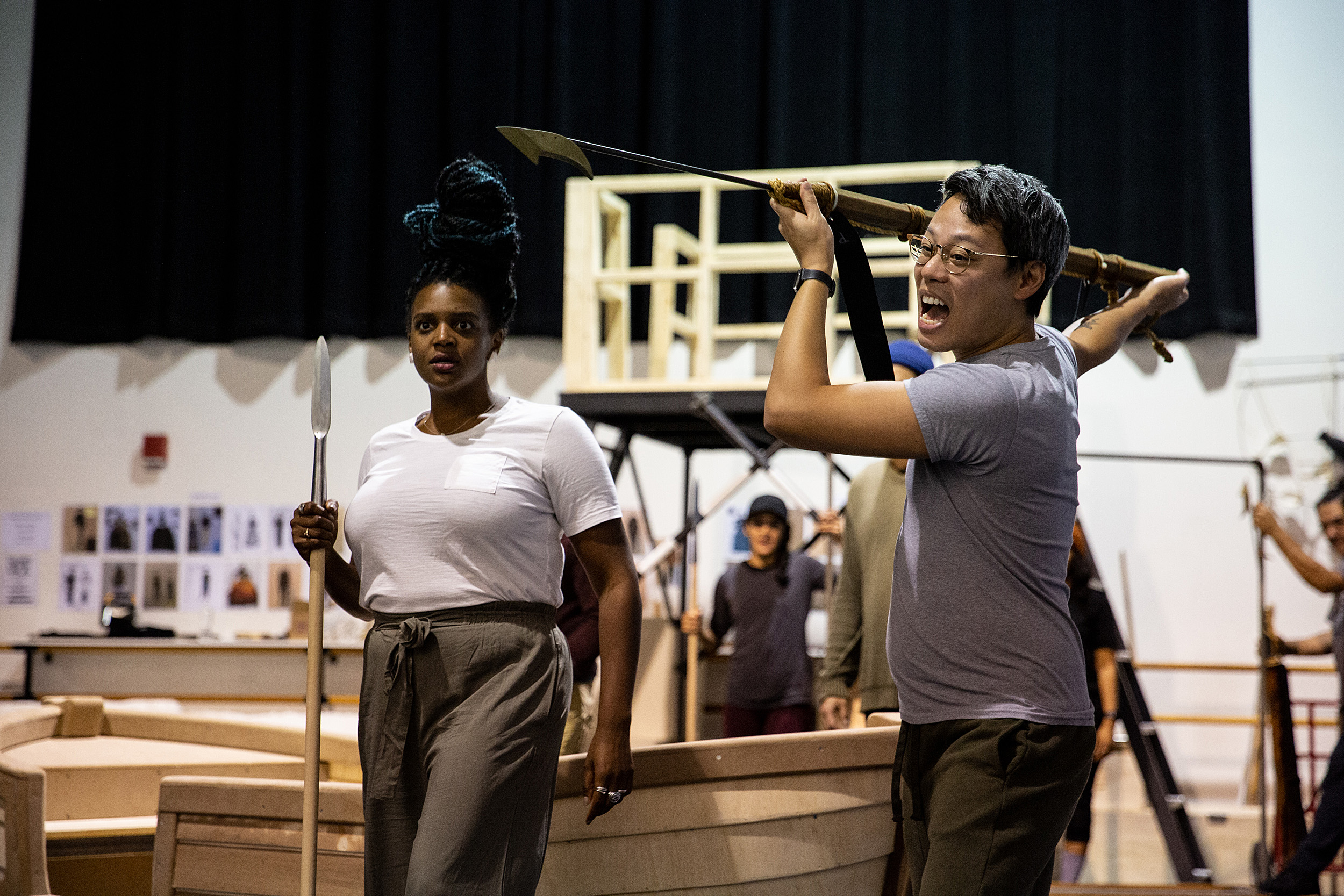 Woman off to the left holds a harpoon, looking surprised. Man in the middle wields the harpoon, yelling.