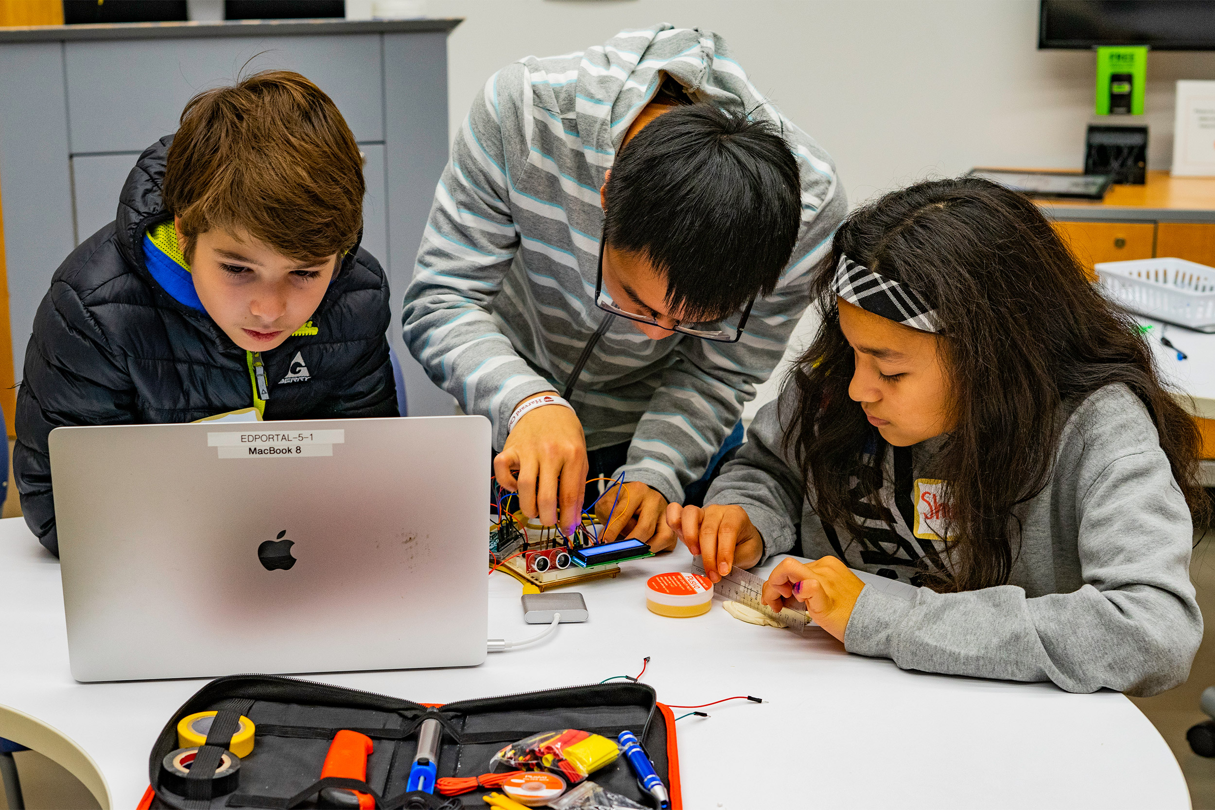 One college student and two youngsters working on circuit board.