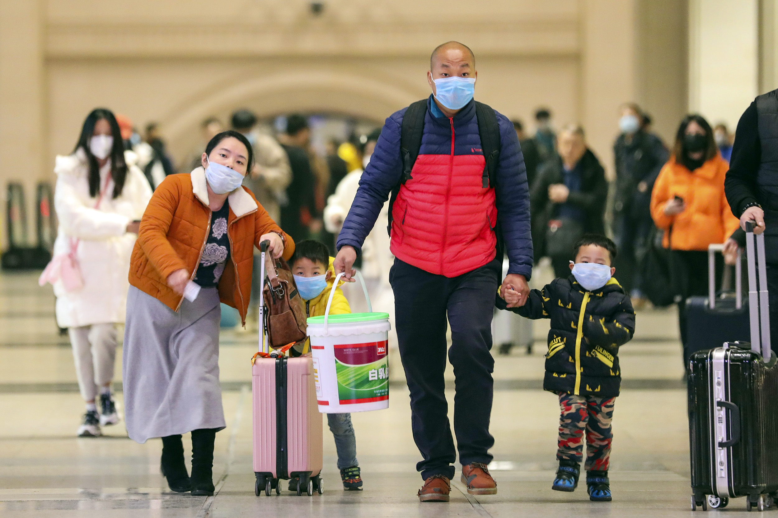 Masked travelers tote luggage in Wuhan in January.