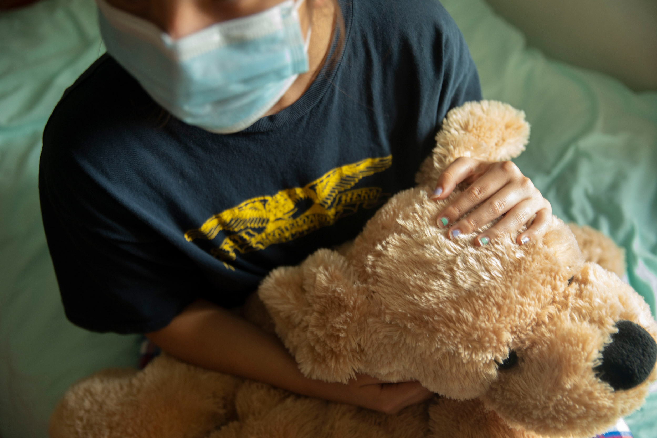 Youngster in mask holding a teddy bear.