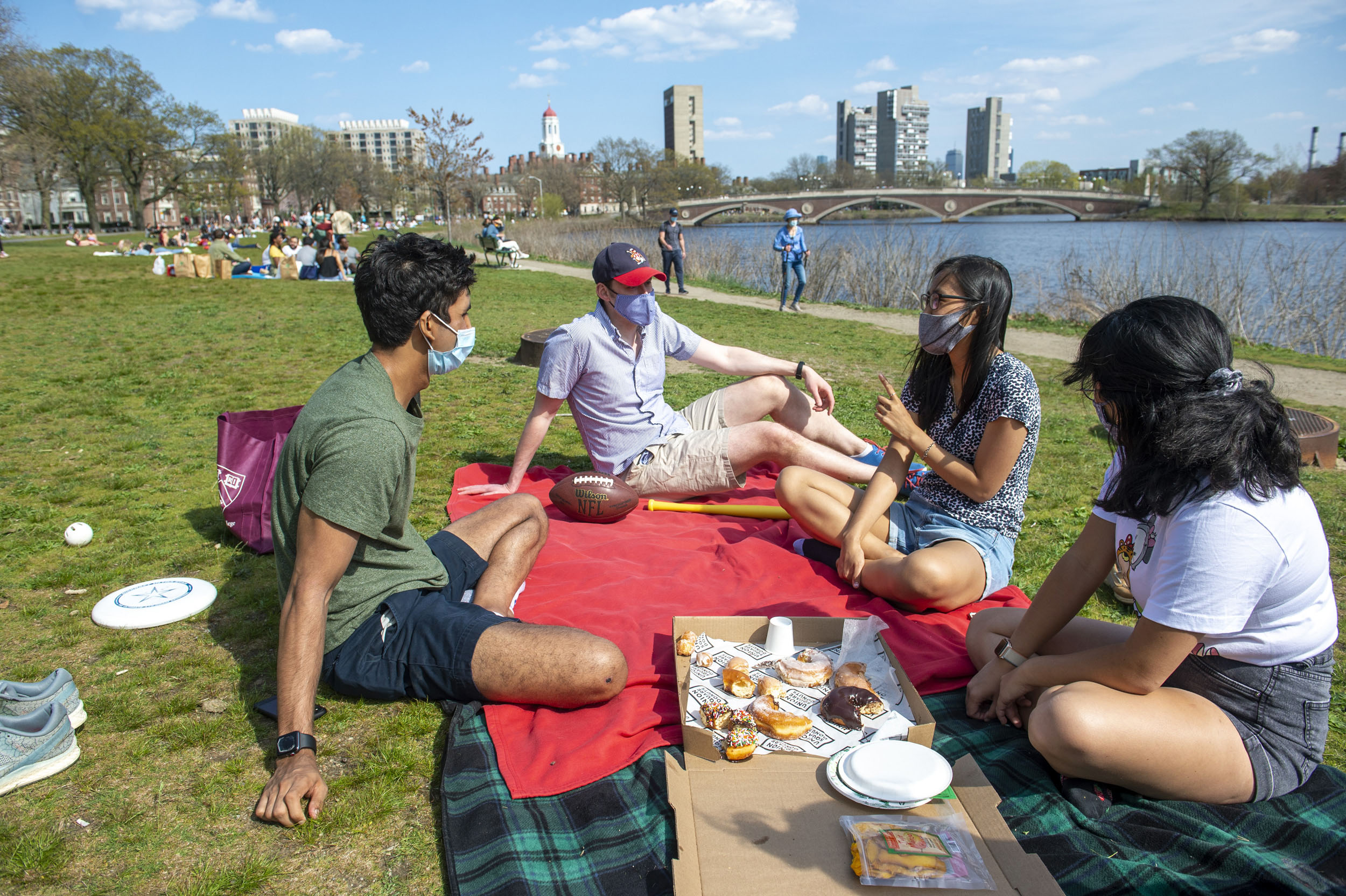 Devin Srivastava ’21 (from left), Brooks Lambert, Nam Hyun Kim ’21, and Ruth Jaensubhakij ’22 gather on the grass between Memorial Drive and the river.