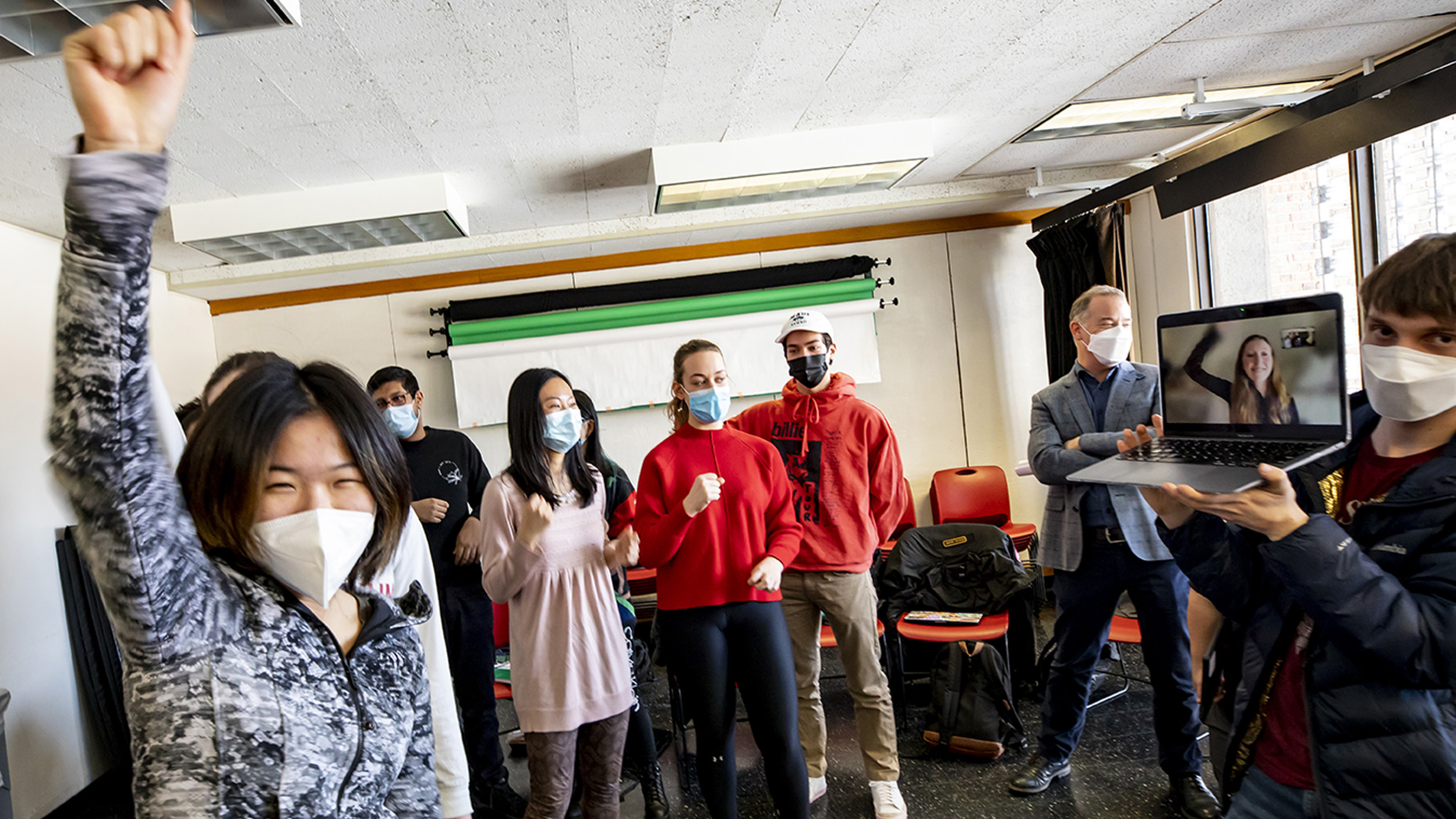 Student raises fist as classmates, including on one Zoom, chant during a musical skit.