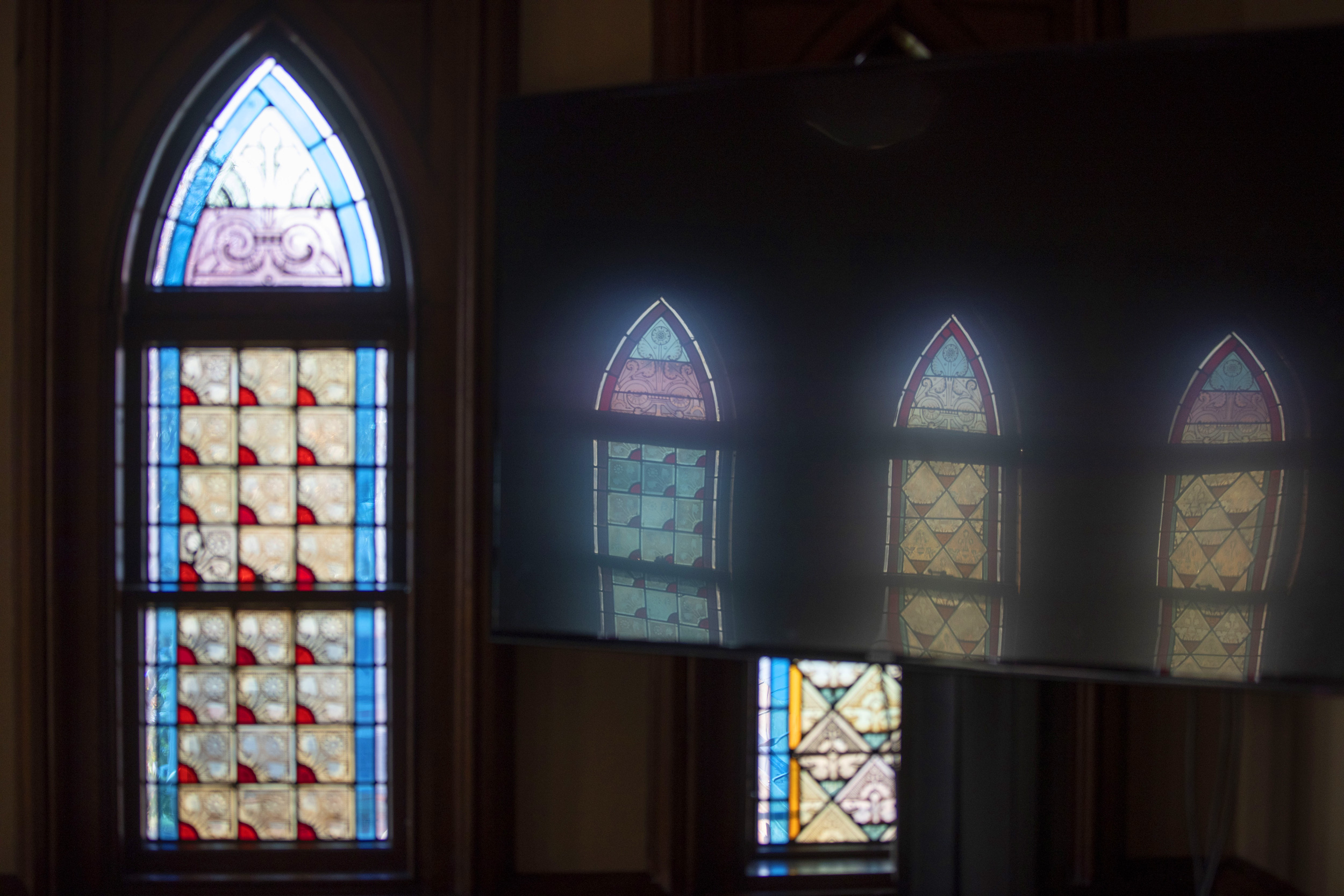 Stained-glass windows cast a reflection on an overhead monitor in Memorial Hall.