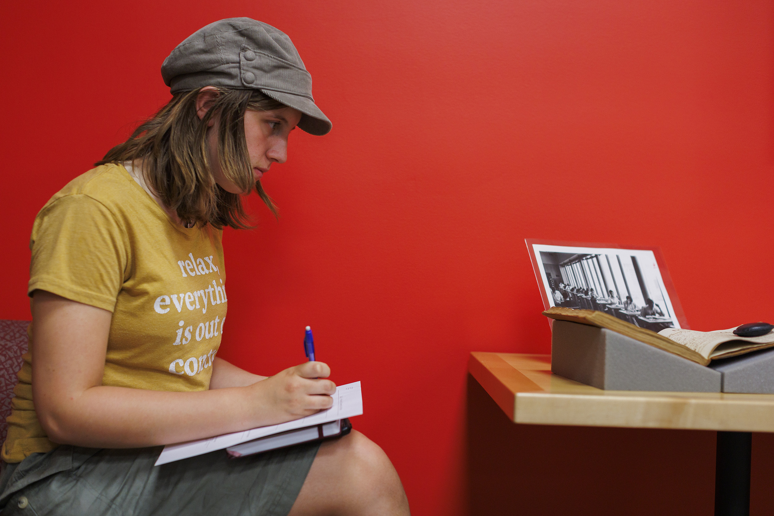 Zoe Groves writing in notebook at desk by an archival image of students at desks.