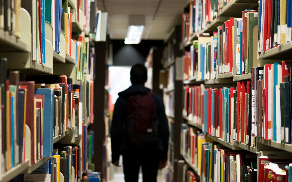 A person in silhouette between library book shelves