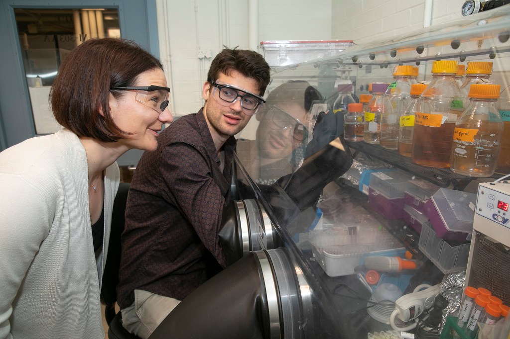 Professor looks over the shoulder of grad student working in the lab