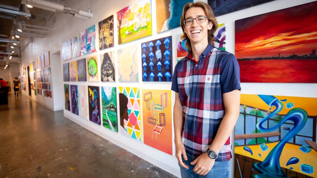 Harvard first year student standing in front of student artwork on wall.