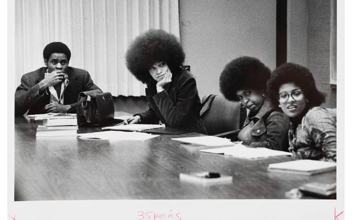 A black and white photo of young Angela Davis sitting at a conference table with three other people