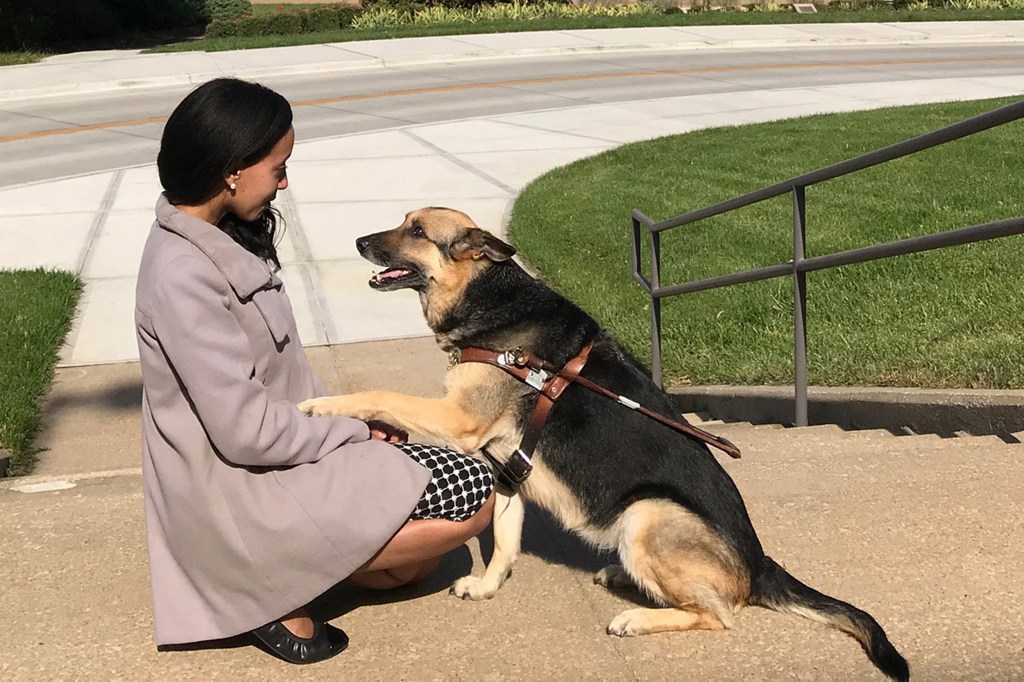 Haben Girma kneels with her dog, who has placed one paw on her knee