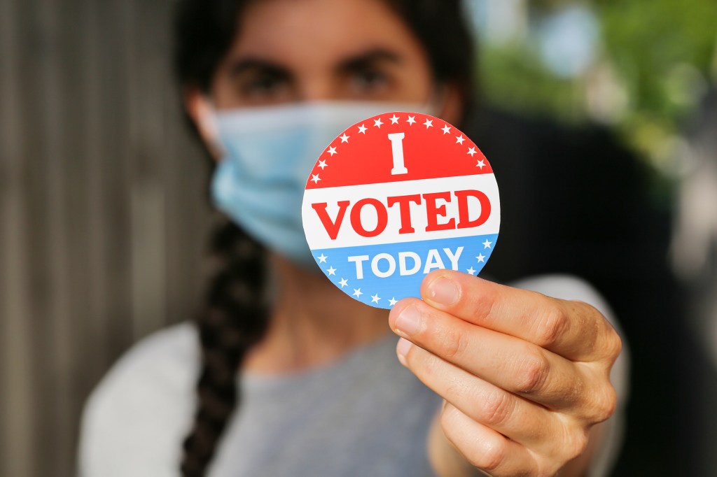 Young woman wearing face mask holding I voted today sticker.