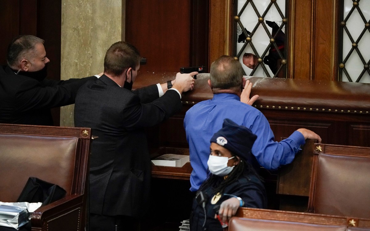 Police with guns drawn watch as rioters try to break into the House Chamber.