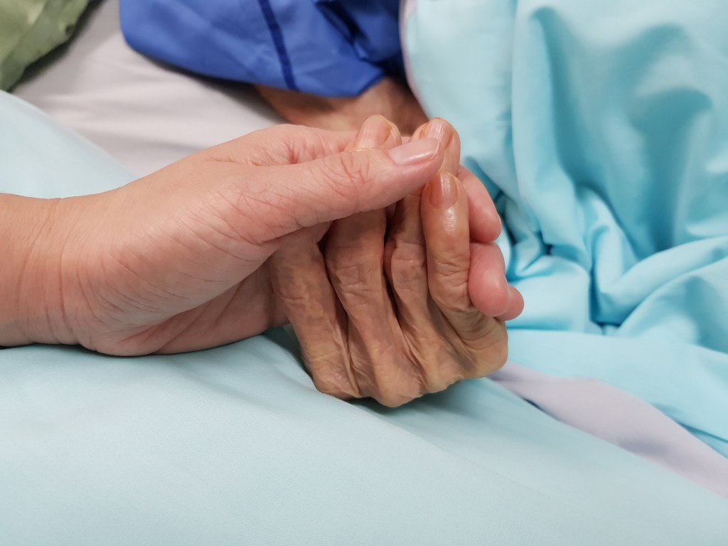 Detail of healthcare worker holding patient's hand.