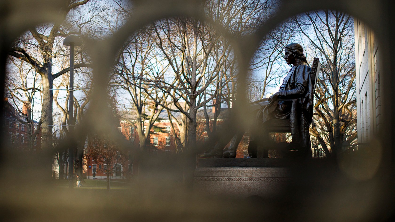 John Harvard statue as seen through the wrought iron rails of University Hall on Harvard's campus. 