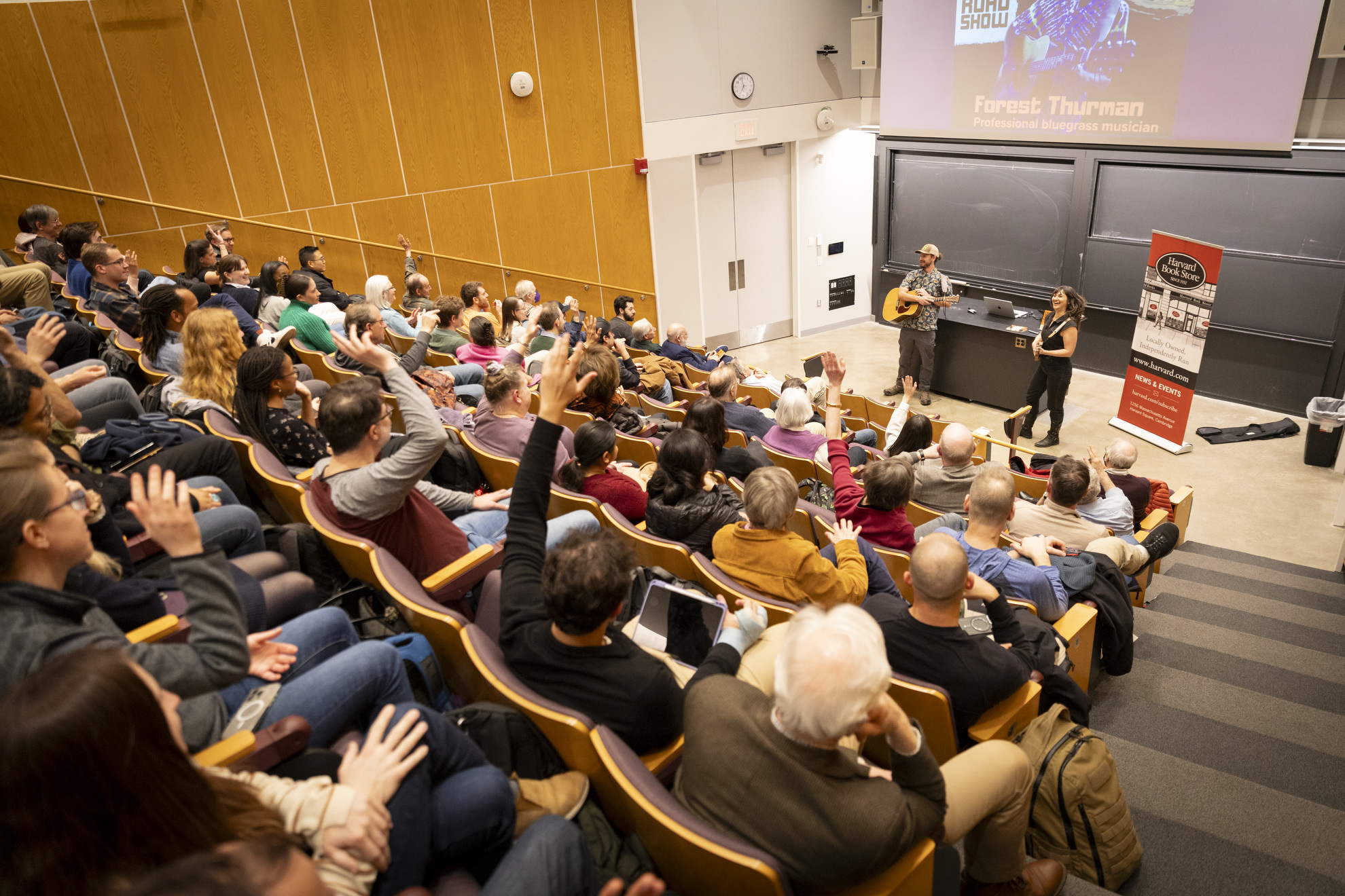 Audience members raise their hands in response to a survey about bluegrass music.