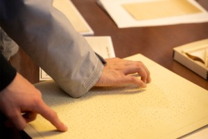 Students test their finger sensitivity on paper with raised letters, shapes and numbers.