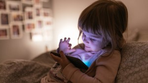 A child sits up in bed and plays on a cell phone.