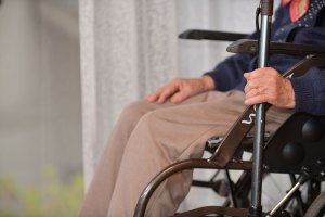 A senior woman sitting in a wheelchair with a cane.