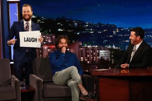 Will Burke holds a "laugh" sign as Zach Galifianakis is interviewed by Jimmy Kimmel.