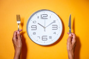 A clock as if it were a plate of food next to a hands holding fork and knife.