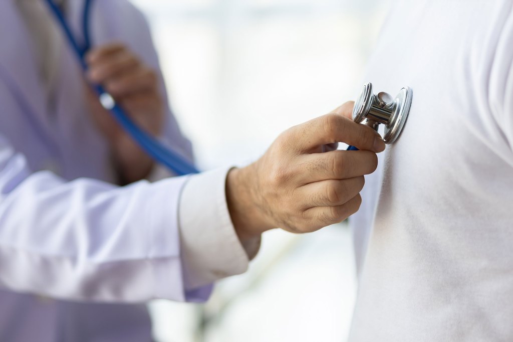 Doctor using stethoscope examining male patient.
