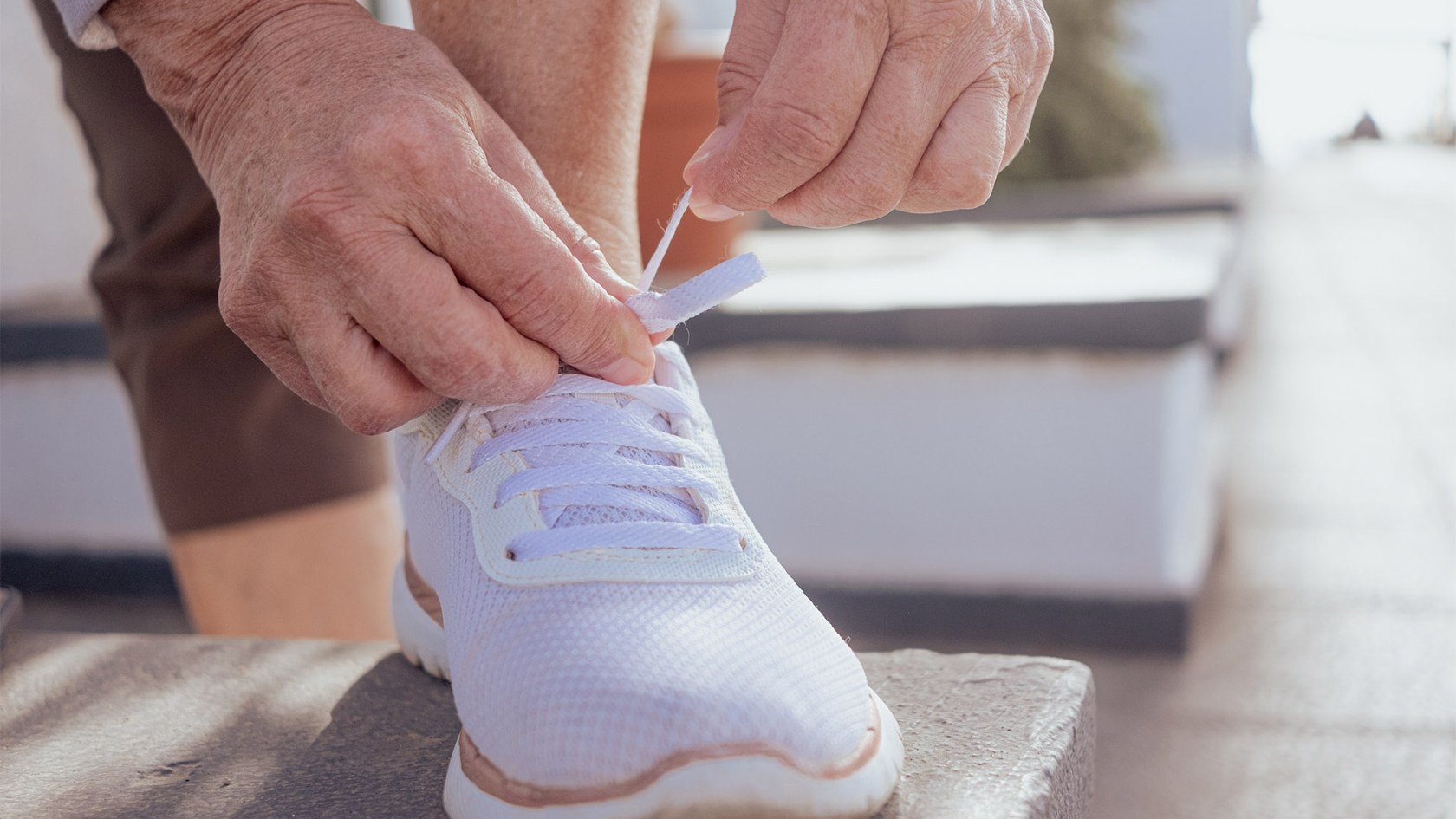 Close-up of woman's hands tying the laces of white sneakers. 
