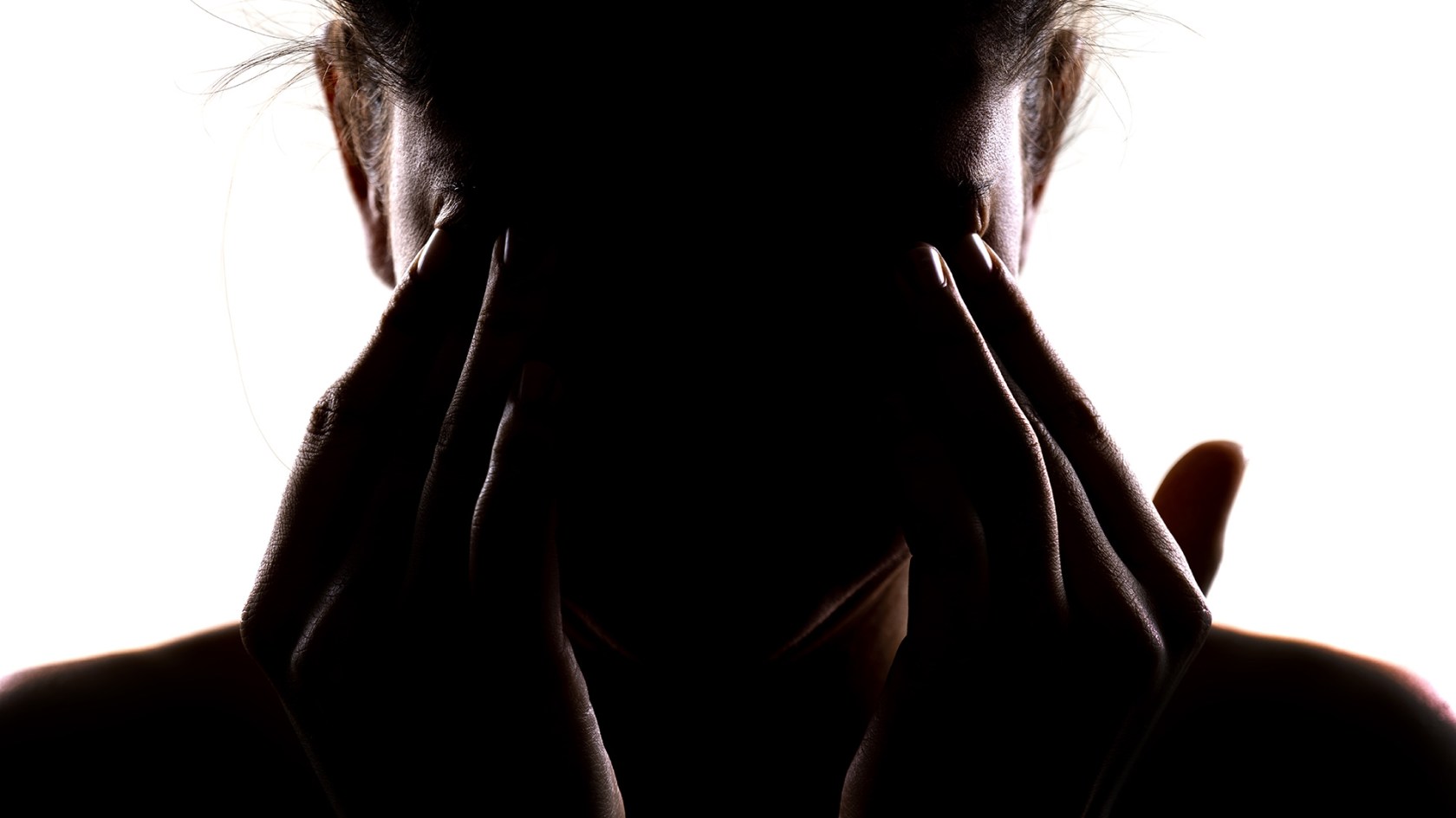 Silhouette of a person holding their head in their hands and rubbing their eyes.