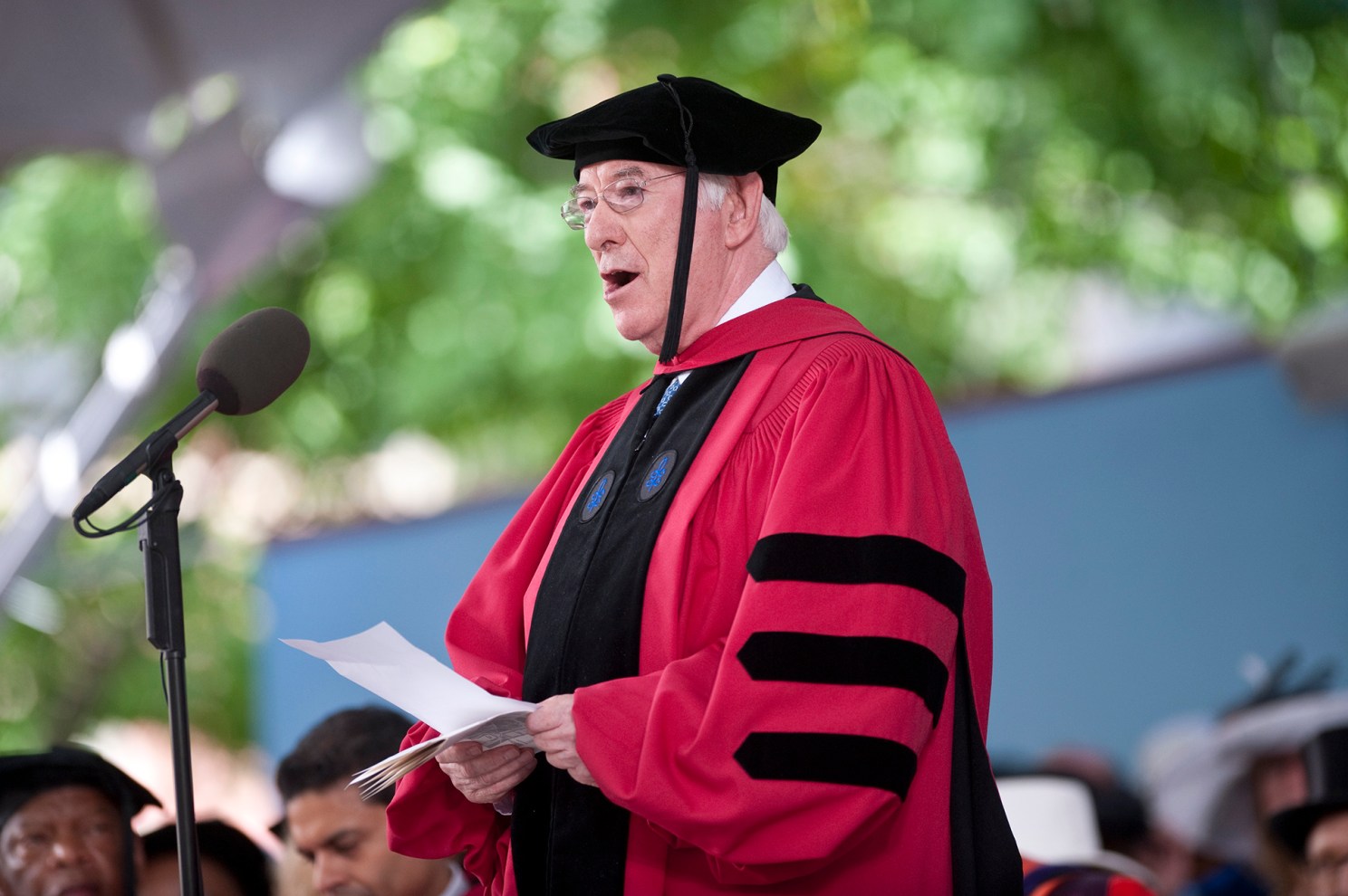 Seamus Heaney reading a poem in Commencement gown and mortarboard at Harvard.