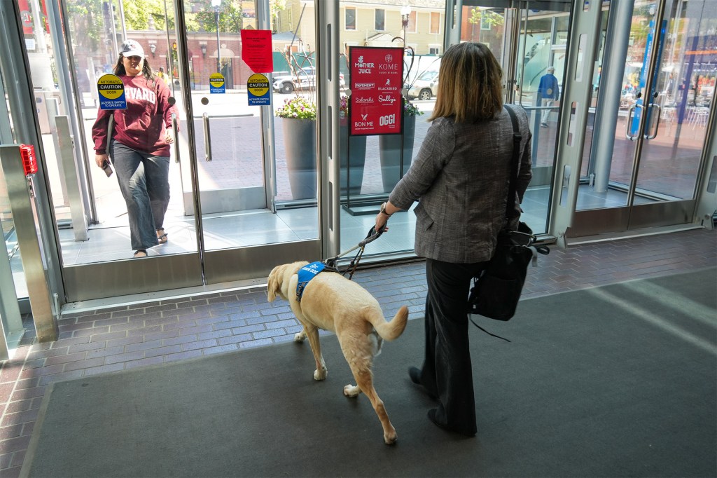 Woman with back to camera, accompanied by service animal, walking toward door of Smith Campus Center.