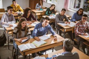 Large group of high school students listening to their teacher.