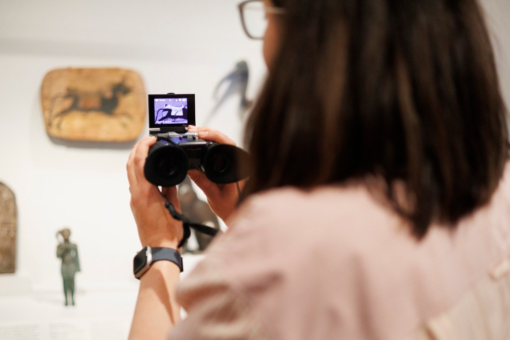 Lisa Barro, an independent conservator and guest lecturer at NYU’s IFA, holds a pair of night vision goggles up to artwork in the Harvard Art Museums. The goggles allow the viewer to see where Egyptian Blue pigment has been used on artworks. 
